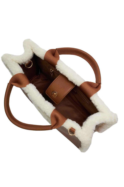 Brown handbag with white shearling lining, top handles and crossbody strap with clasps