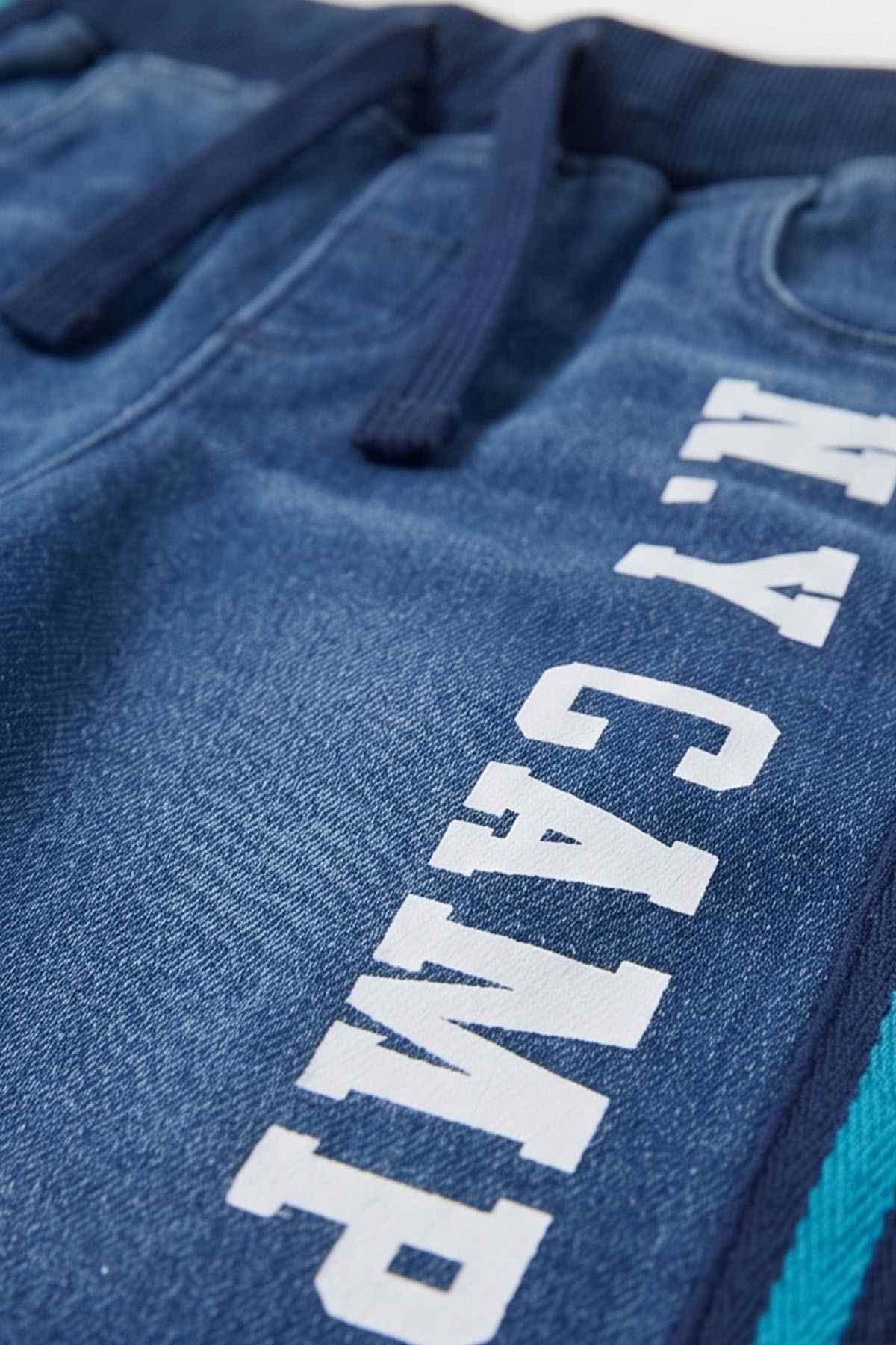 Blue denim-style pants with vertical white text print and teal side stripe