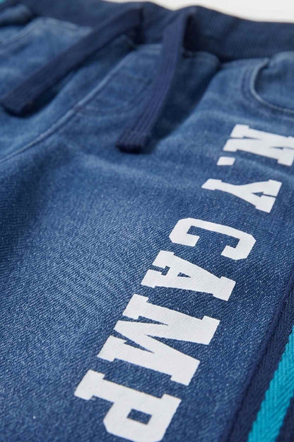 Blue denim-style pants with vertical white text print and teal side stripe