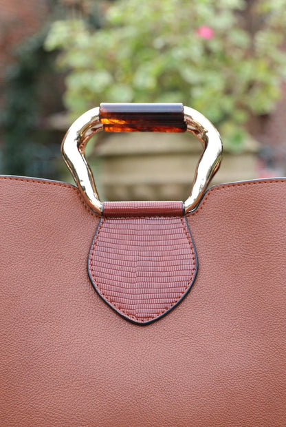 Brown handbag close-up of metal handle clasp and front strap detail