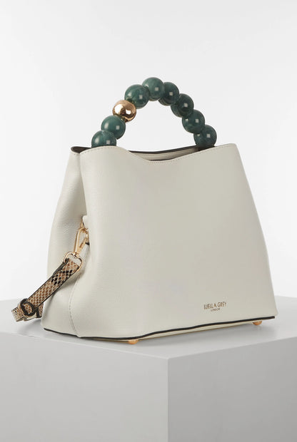 White bucket bag with green beaded handle and leopard-print strap detail; curved silhouette