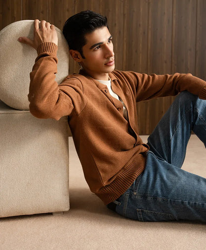 Men's fitted brown cardigan with ribbed cuffs, seated pose with jeans