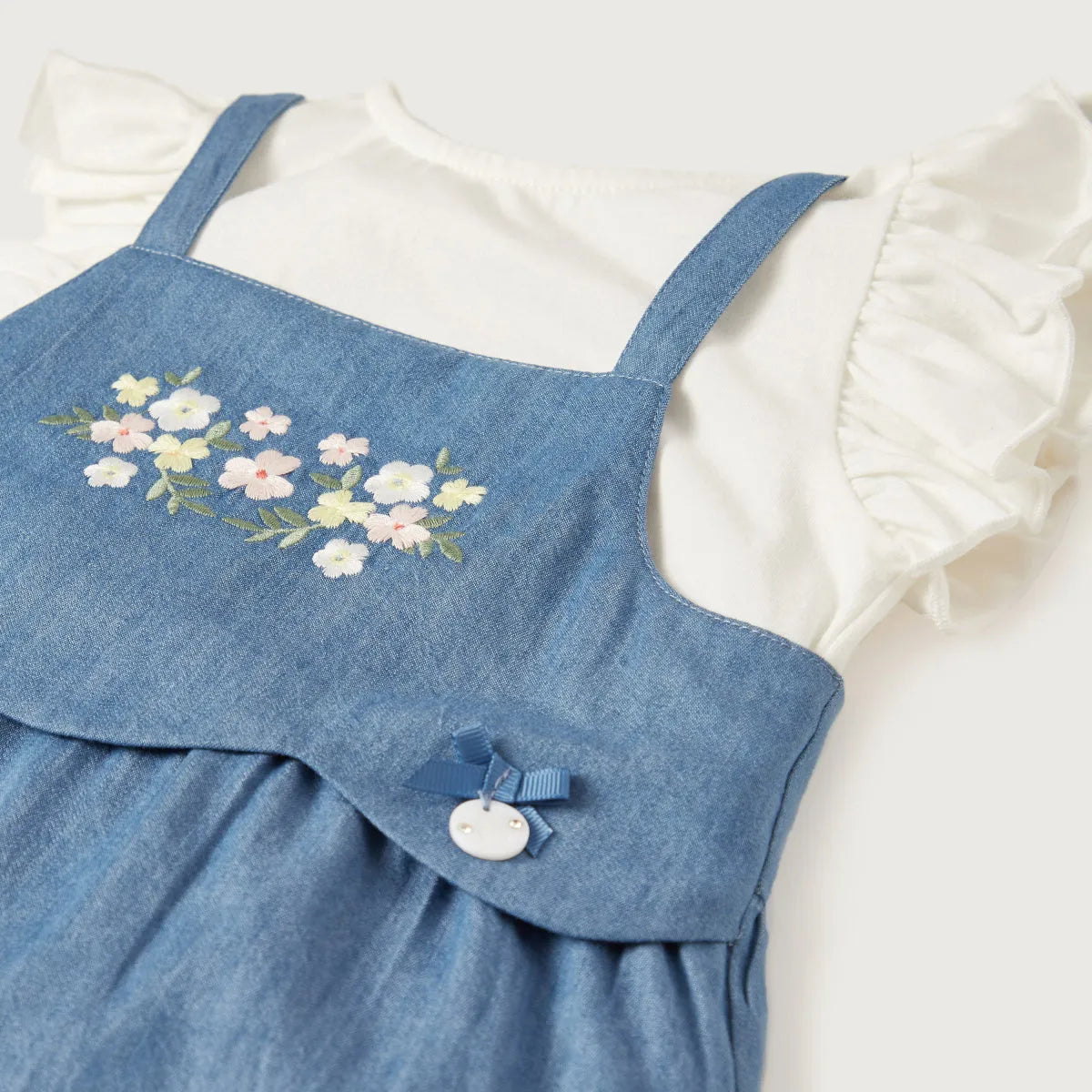 Blue denim romper detail with floral embroidery, button closure, and adjustable strap