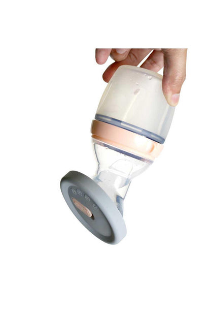 Grey silicone breast pump cap with beige valve insert, held above bottle