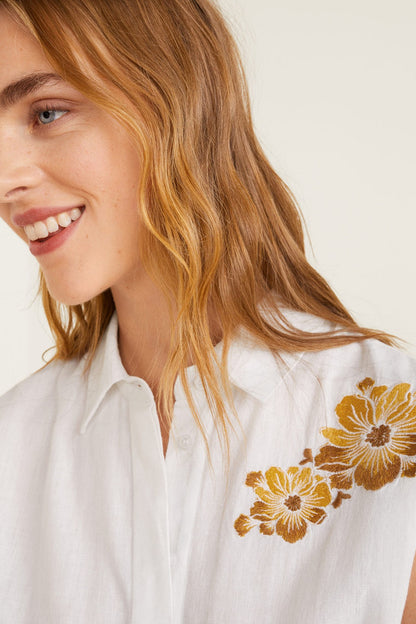 White blouse with golden floral embroidery and buttoned collar detail