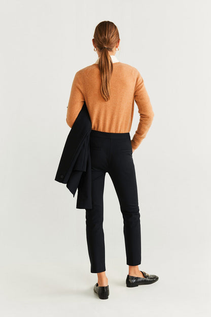 Black slim trousers with tan sweater and black blazer draped over shoulder