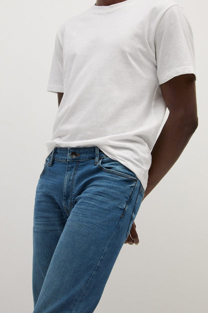 Blue denim jeans showing side seam and button closure at mid-rise waist