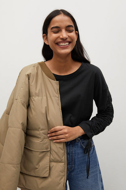 Black long-sleeve top under beige utility jacket, side drawstrings