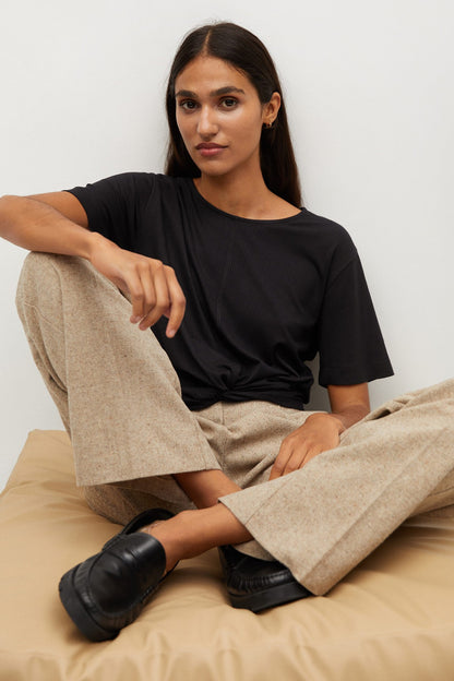 Black knotted short-sleeve top with beige wide-leg trousers, seated close-up