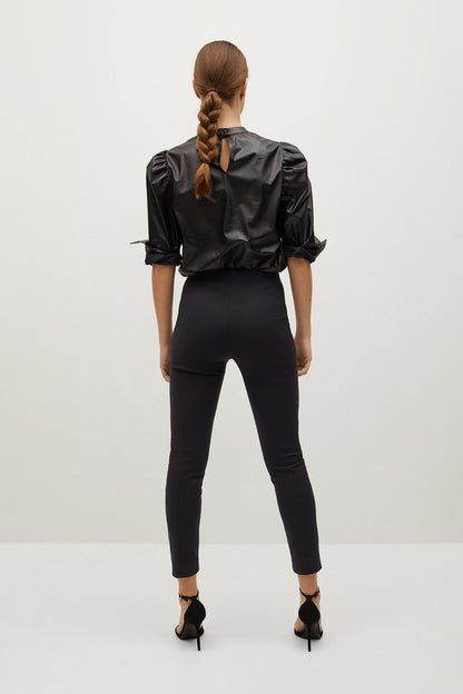 Black high-neck blouse with puff sleeves and skinny black trousers, full-length view