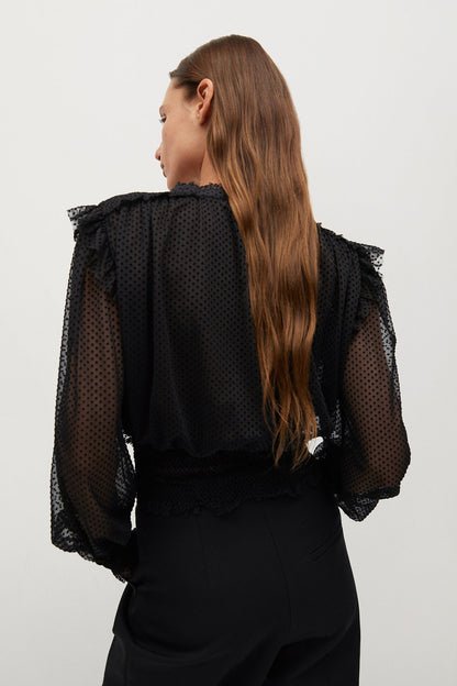 Black sheer dotted blouse from back view with ruffle shoulders and long sleeves