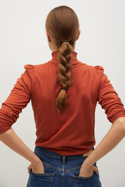 Back view rust orange long-sleeve knit turtleneck top with ruffled shoulders
