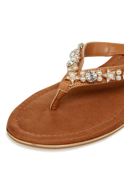 Close-up of tan thong sandal with embellished ankle strap and pearls