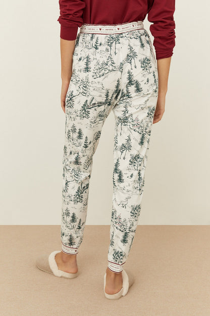 Off-white pajama pants with green pine forest print, red drawstring waist, tapered legs