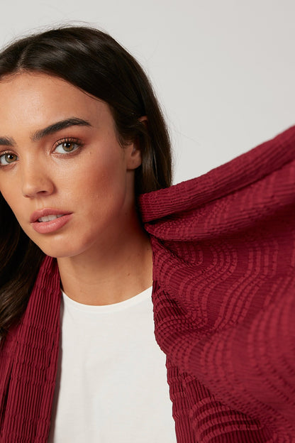 Woman wearing burgundy textured scarf with pleated stripe pattern along neckline